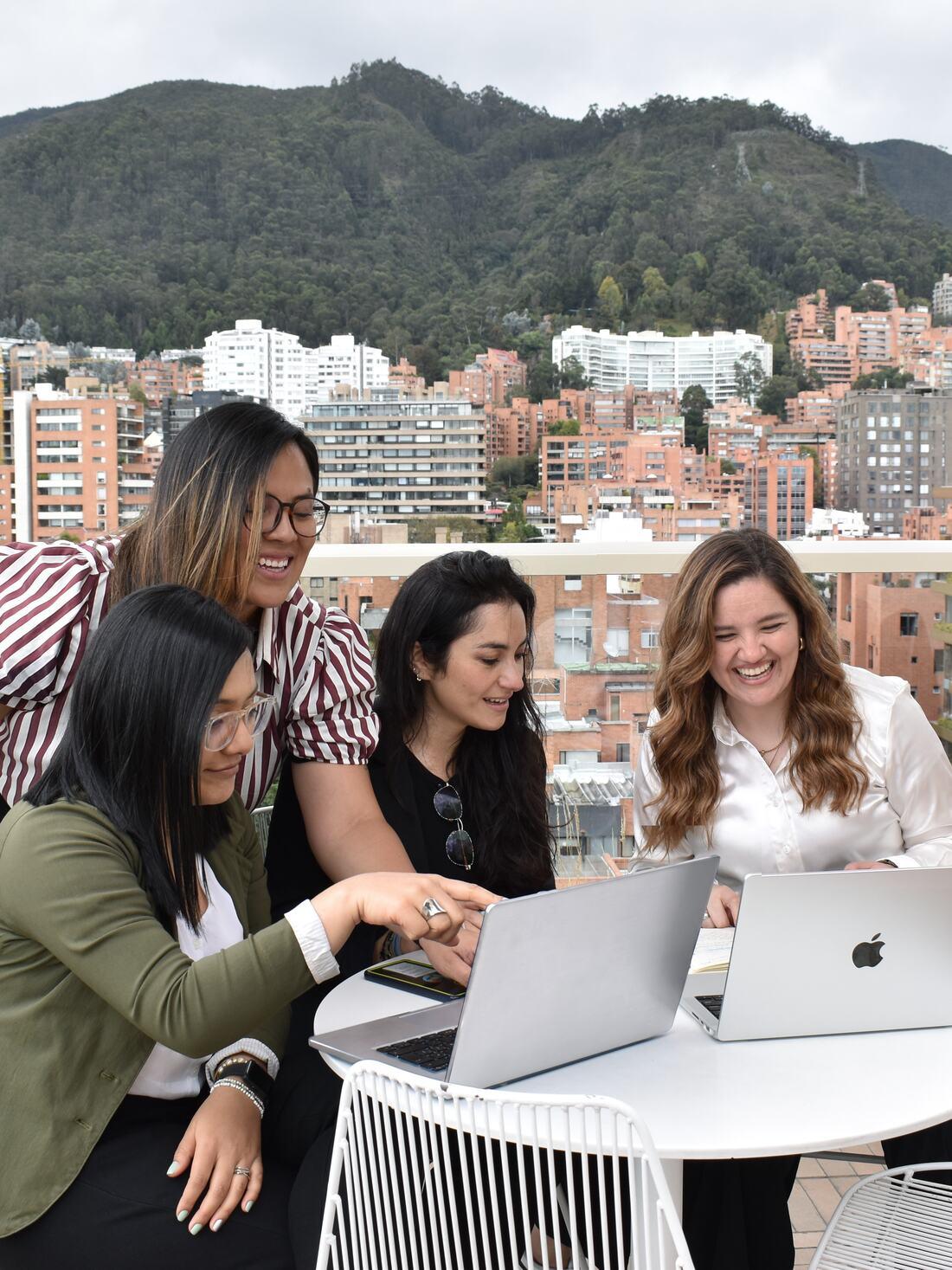 Four members of the Moraich team reviewing a laptop together on the office terrace, with Bogotá behind them